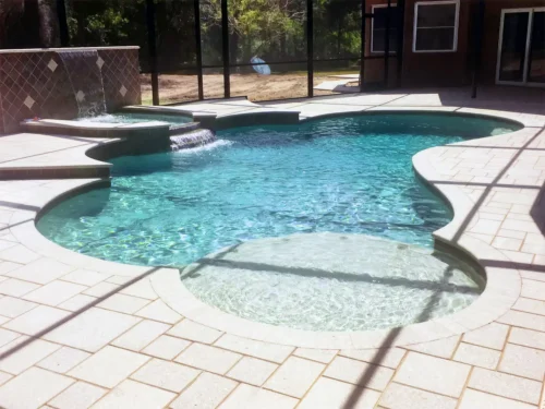 Freeform custom built pool with sun shelf, spillover spa, and water feature