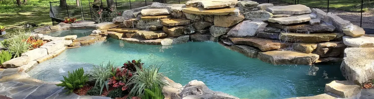 Freeform lagoon style pool with spa, bubblers, and waterfall feature over stacked rocks