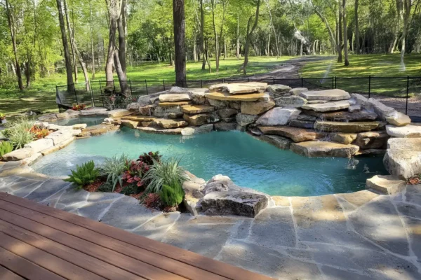 Freeform lagoon style pool with spa, bubblers, and waterfall feature over stacked rocks