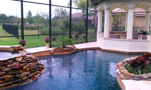 Freeform pool with natural rock waterfall, spillover spa, rock planters, and outdoor kitchen