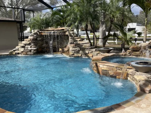 Freeform pool with rock grotto waterfall, spillover spa, and fire bowls