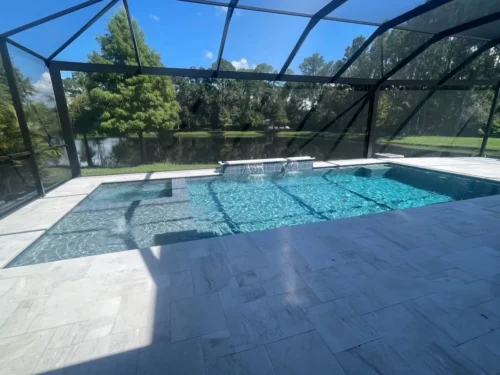 Geometric pool and spa with sun shelf and multiple water features inside screened enclosure.