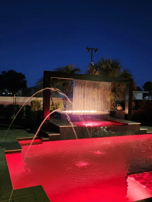 Geometric pool with LED lighting, water, and fire features at night.