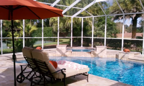 Geometric pool with spillover spa inside screen enclosure.