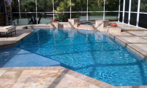 Geometric pool with spillover spa & sun shelf inside screen enclosure .