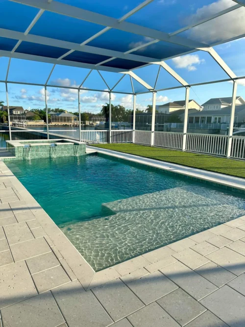 Geometric pool with spillover spa & sun shelf inside screen enclosure.