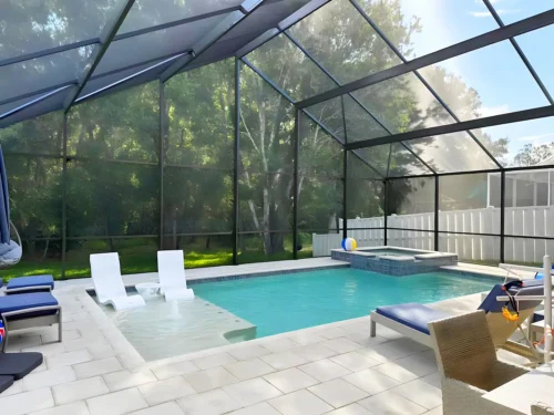 Geometric pool with sun shelf, bubblers, & spillover spa inside screen enclosure.