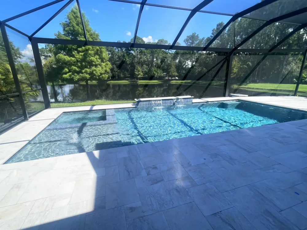 Geometric pool with sun shelf, spa, & water features inside screen enclosure.