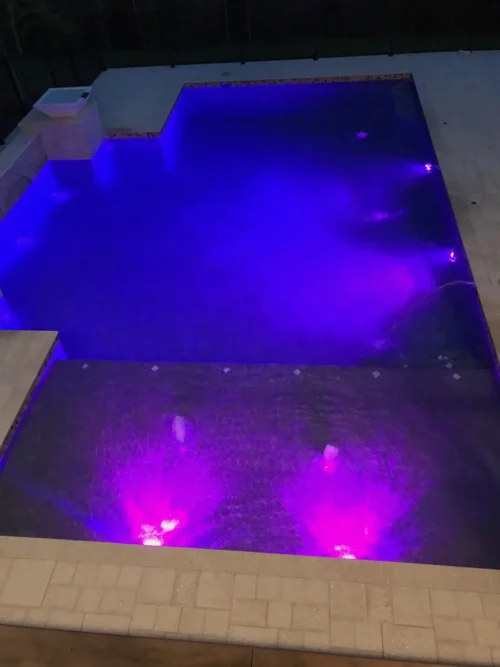Night view of custom built geometric pool with LED lighting and sun shelf