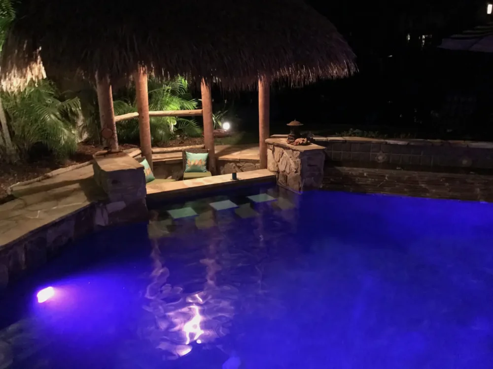 Night view of custom pool with LED lighting, swim-up bar, and water features at night from a custom pool builder